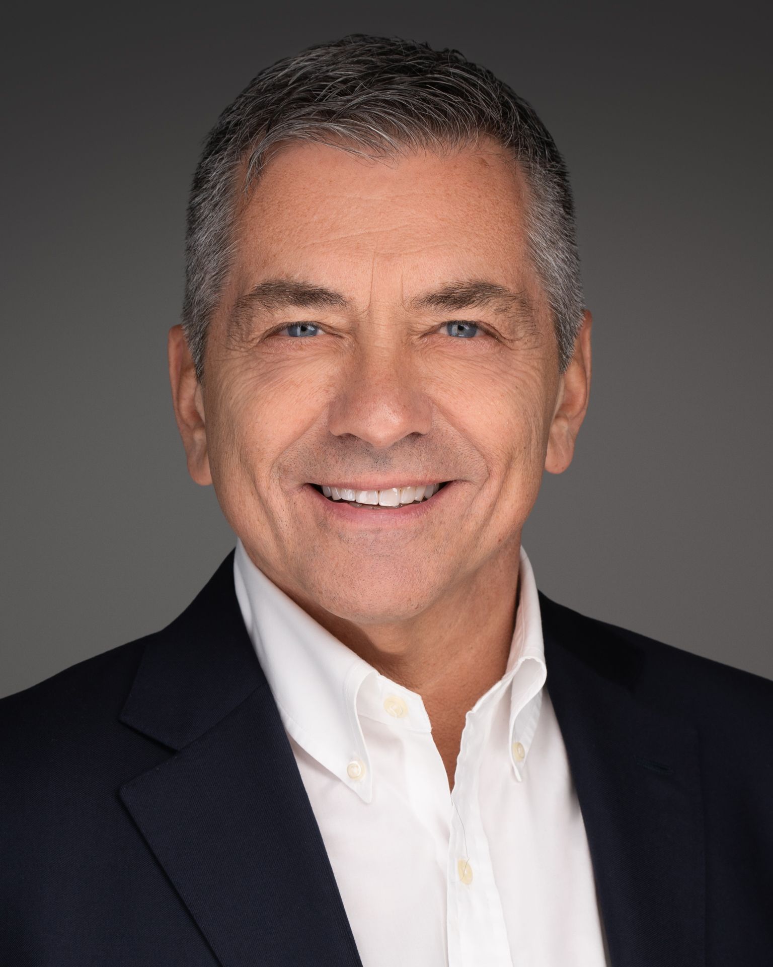 Corporate headshot of a male professional in a navy blazer and white dress shirt against a neutral studio background, captured by Malena Vazquez for Art of Portraits – Miami Headshots & Portraits.