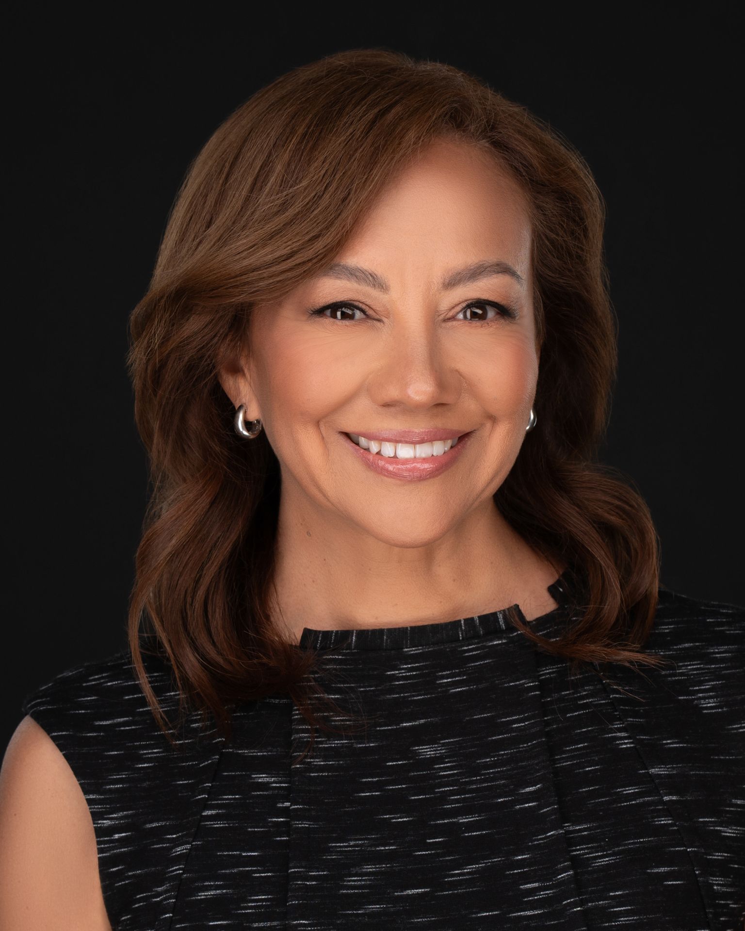 Professional female executive headshot with styled brown hair and dark textured dress, photographed in studio lighting by Malena Vazquez for Art of Portraits – Miami Headshots & Portraits.