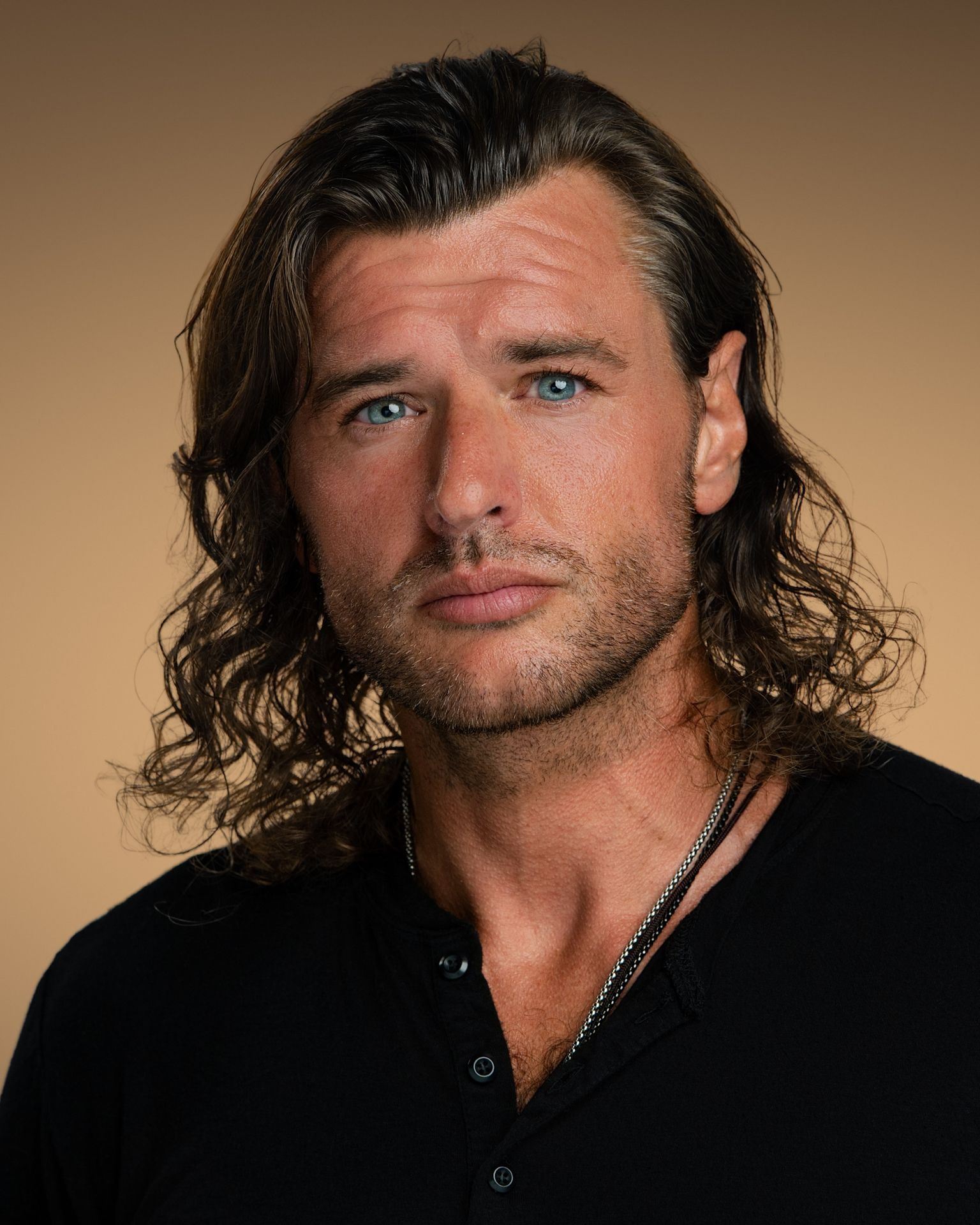 Professional headshot of Andy Brodhag with long wavy hair, wearing a dark blazer and patterned shirt against a neutral background.