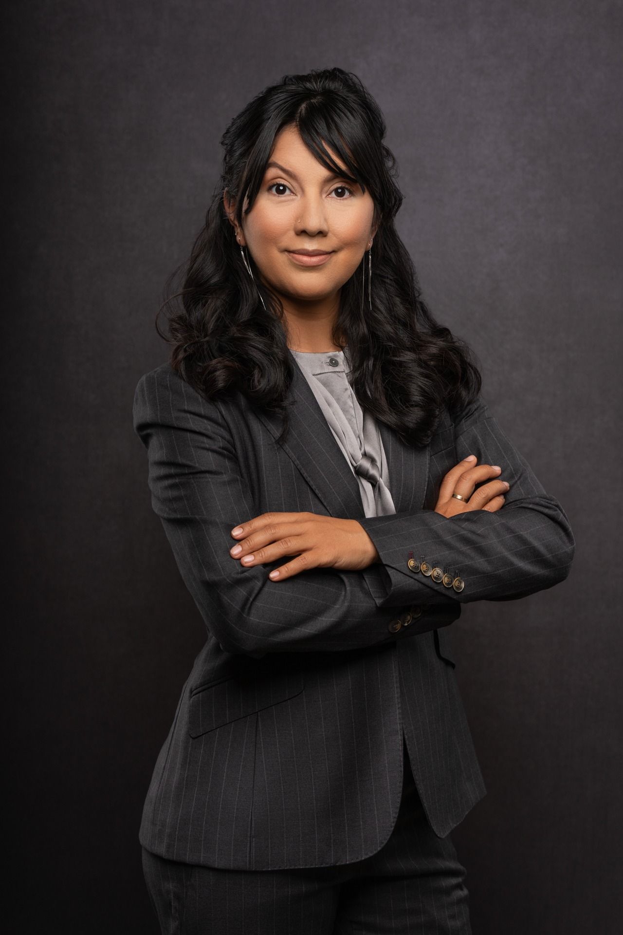 Professional studio portrait of an individual wearing a dark pinstripe business suit, standing with arms crossed against a dark textured backdrop, representing corporate branding photography.