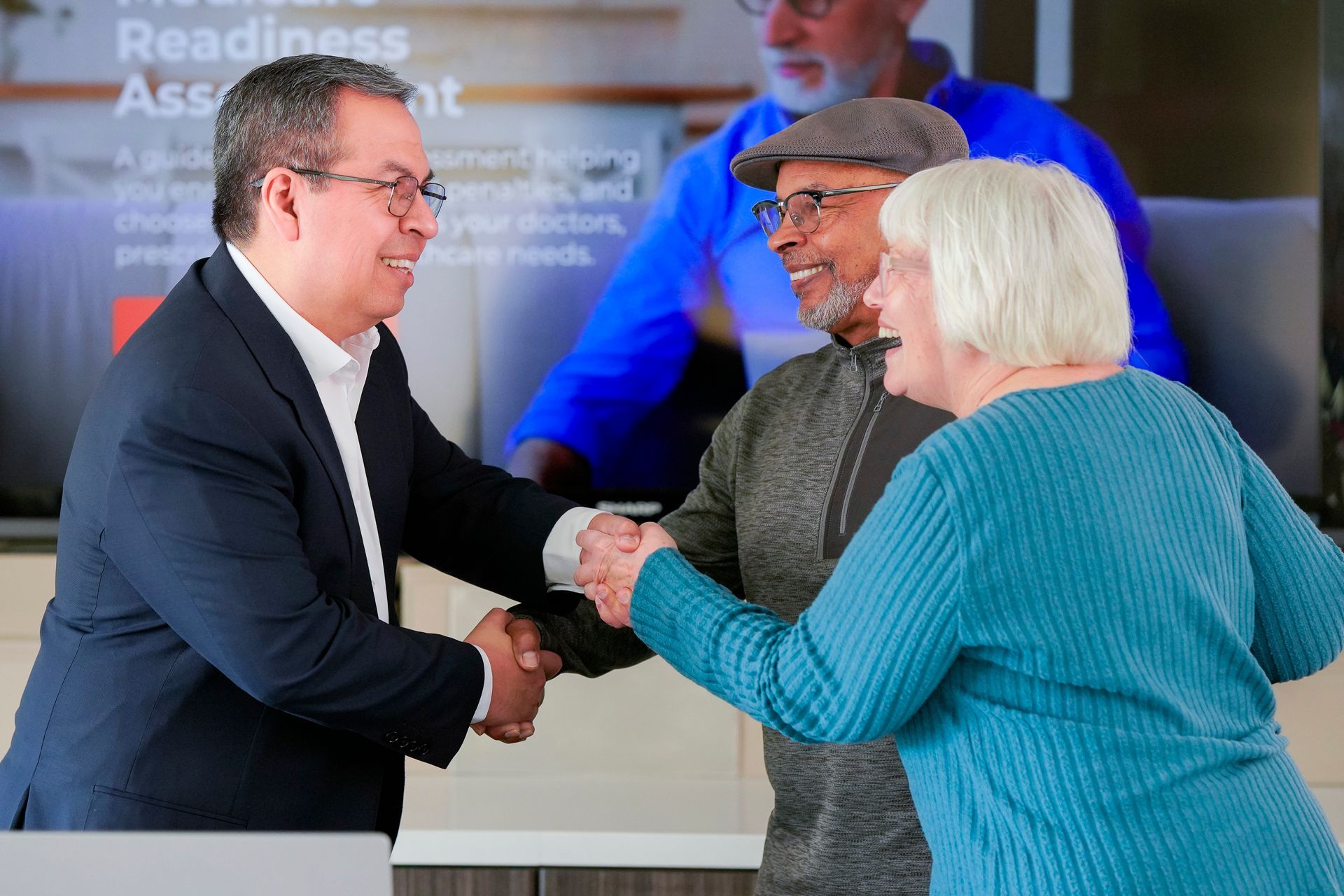 Business professional shaking hands with a couple across a desk during an in‑person consultation.