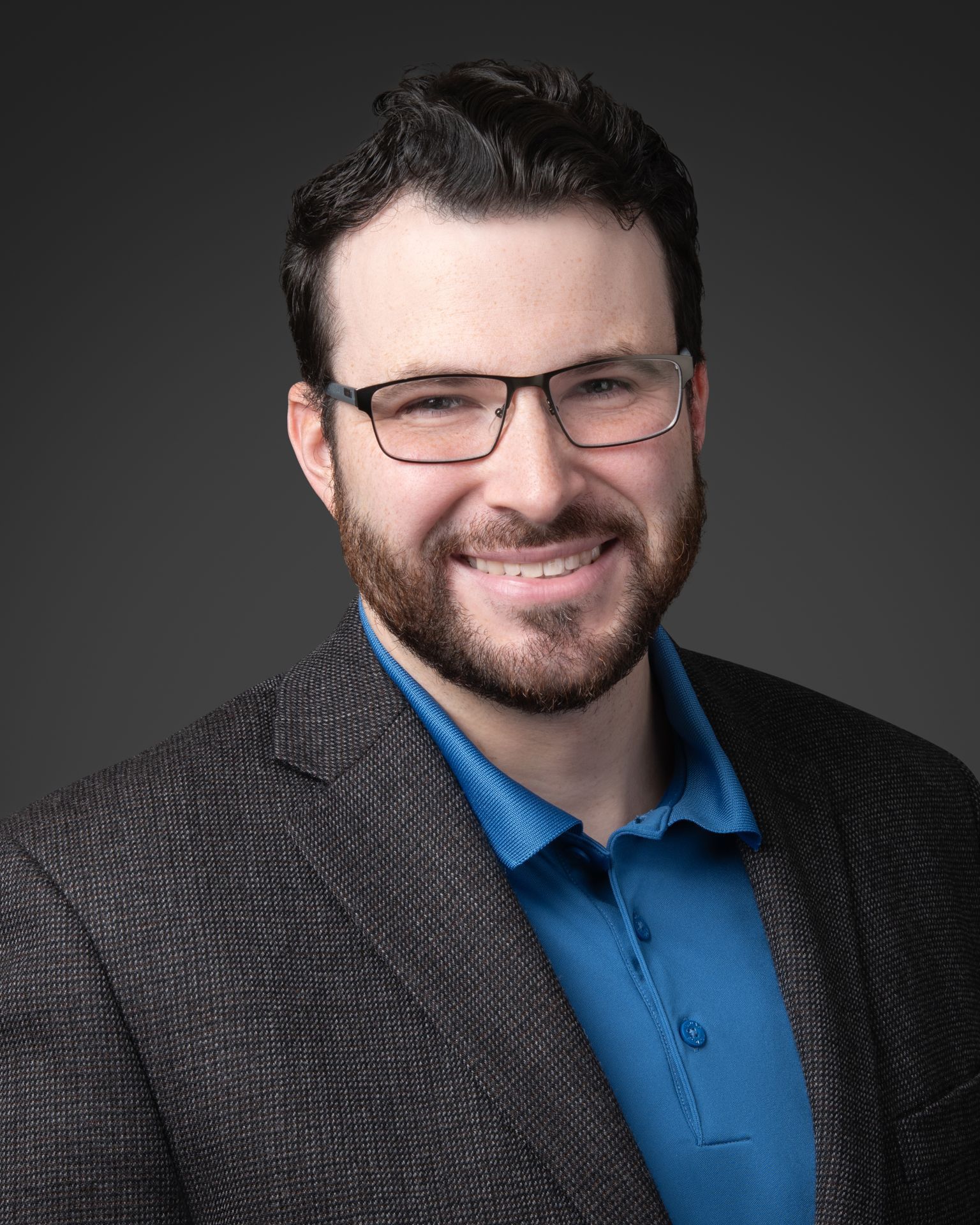 Modern professional headshot of a Philadelphia corporate professional wearing a blazer and blue shirt, studio lighting with dark backdrop.