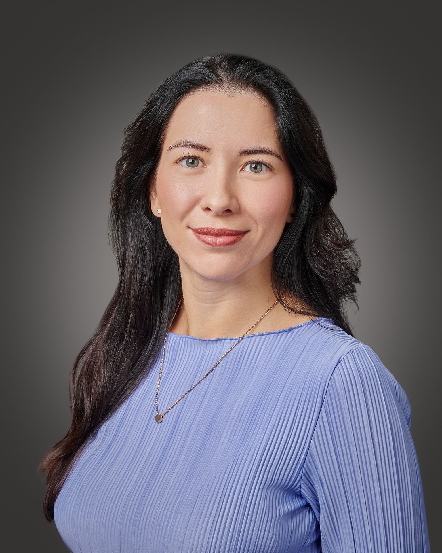 Studio headshot of a Philadelphia professional woman wearing a light blue blouse, modern corporate portrait with dark gray background.