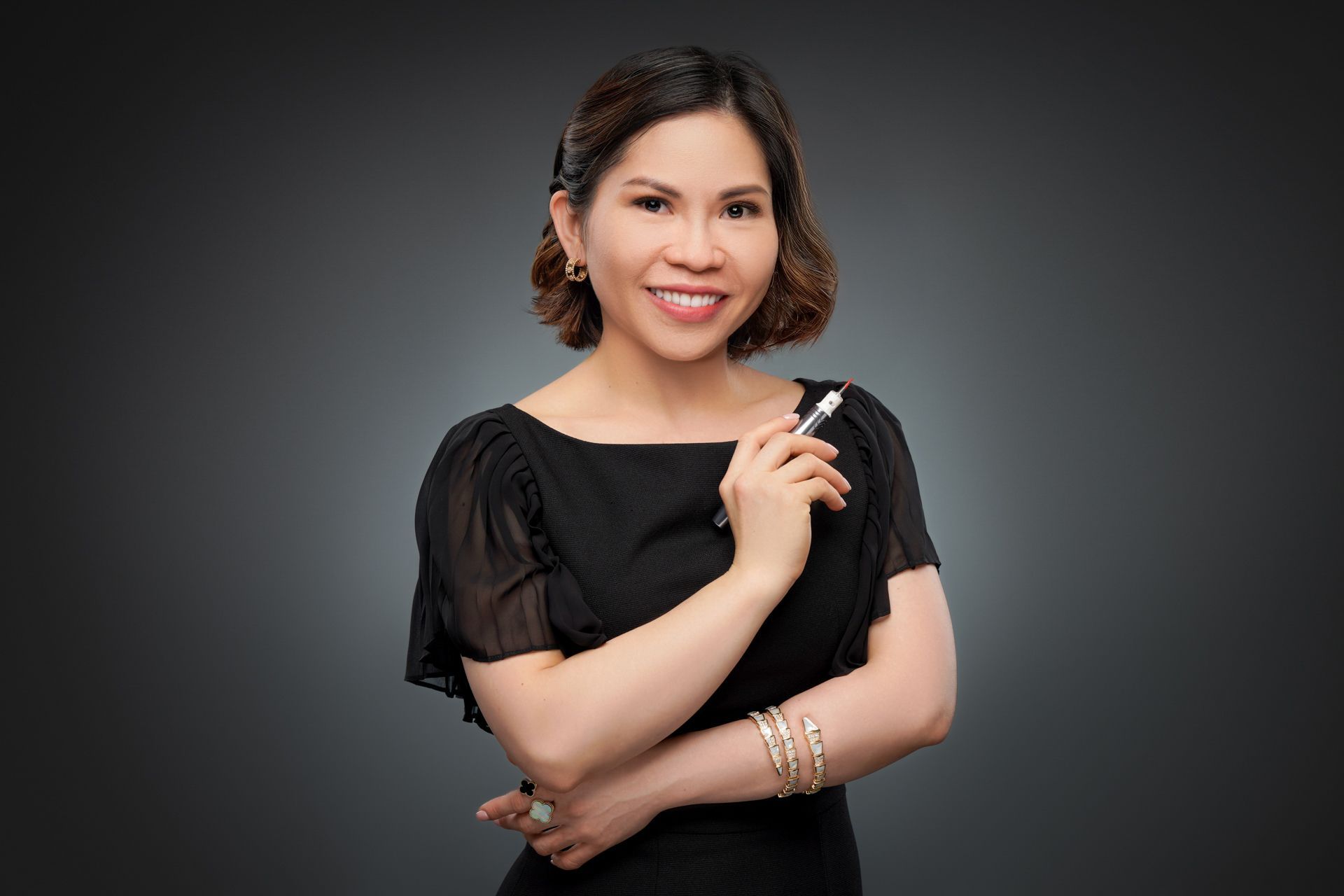 Woman in black top smiling, holding a pen, against a gray gradient background.