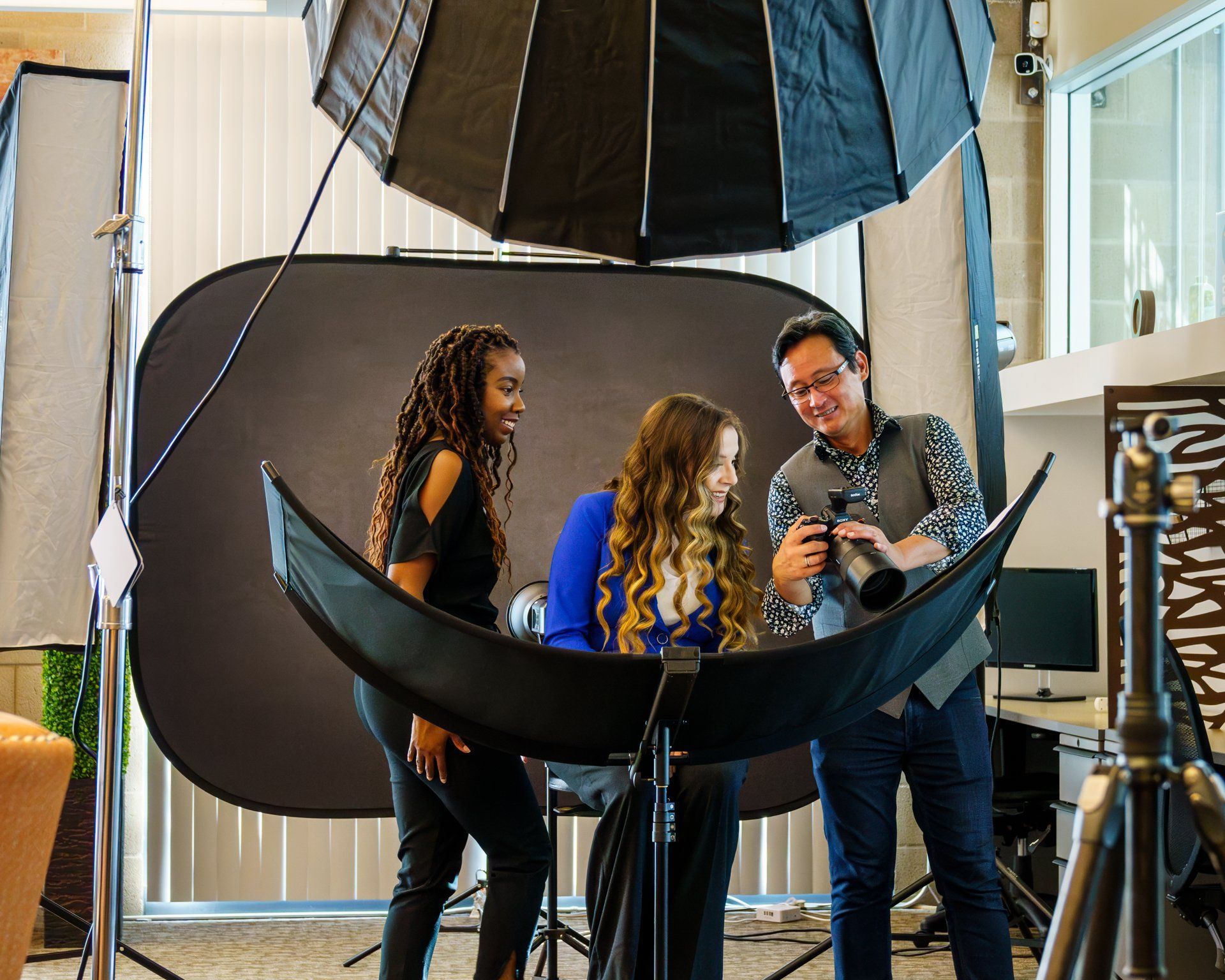 Three people in a photo studio with softbox lights, backdrop, and camera gear preparing for a professional photoshoot.