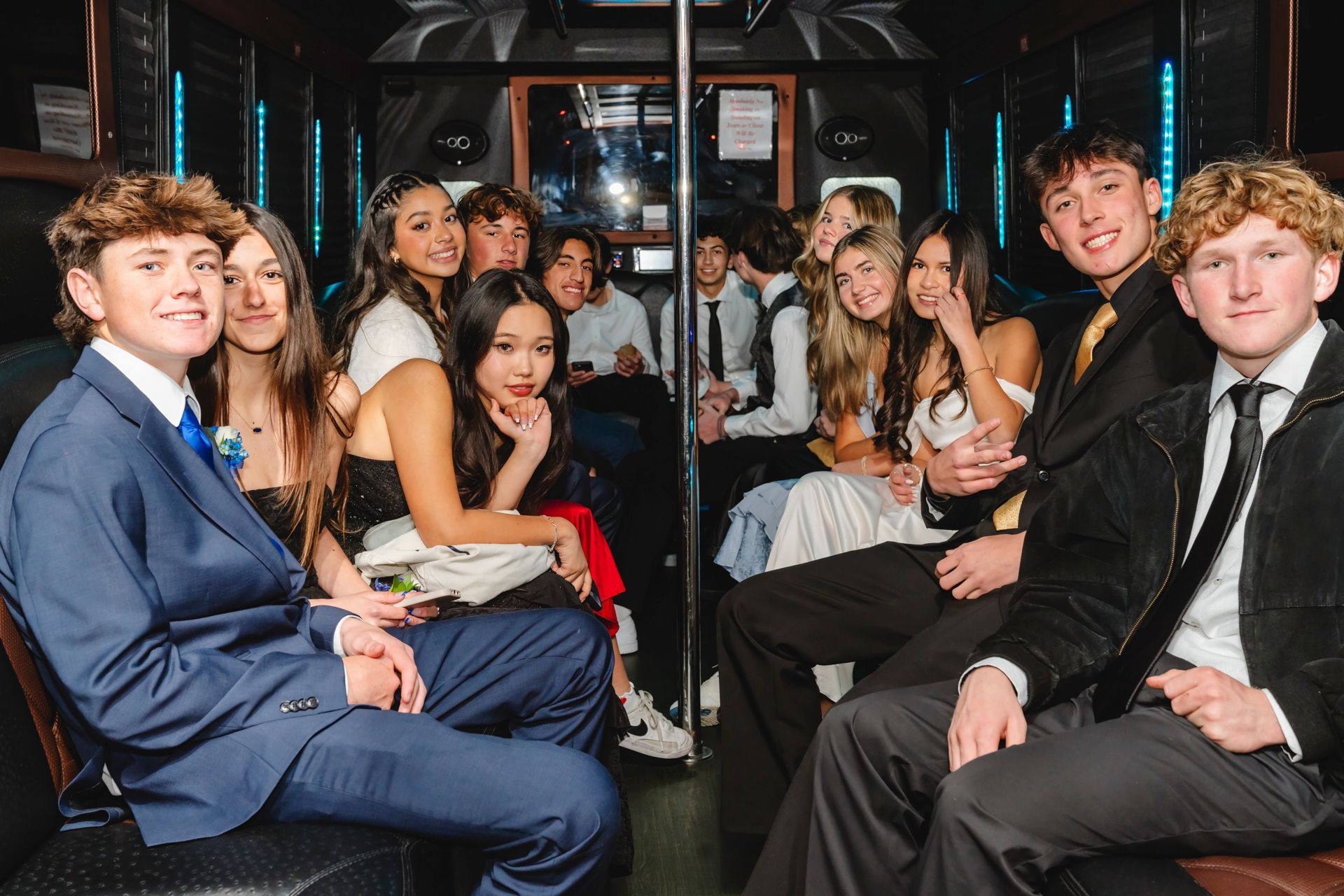 Group of people dressed in formal attire sitting inside a party bus with wood paneling and bright lights, creating a festive and elegant atmosphere.