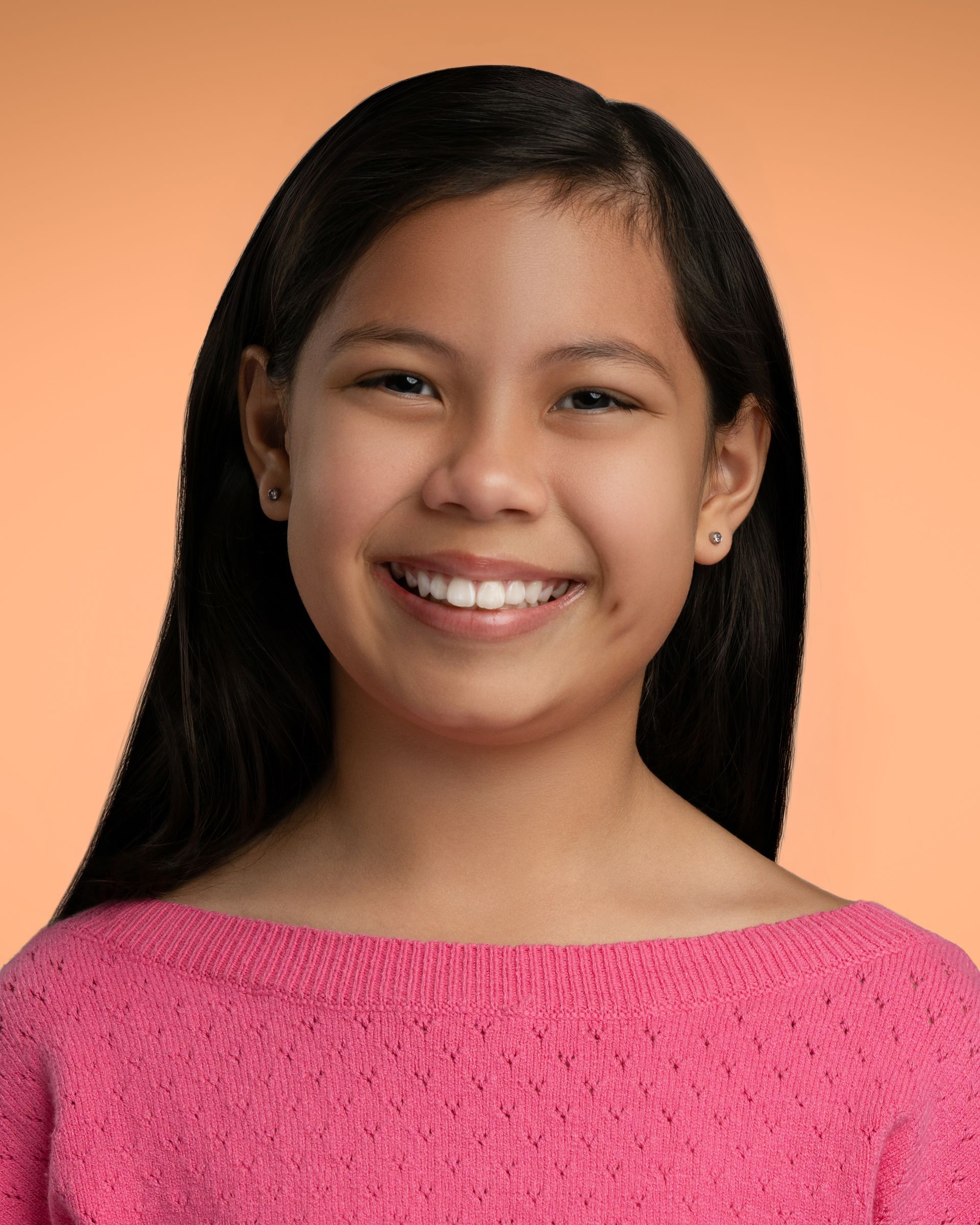 A person wearing a bright pink textured sweater is posed for a studio portrait against a smooth orange backdrop, with long dark hair neatly styled and resting over the shoulders.