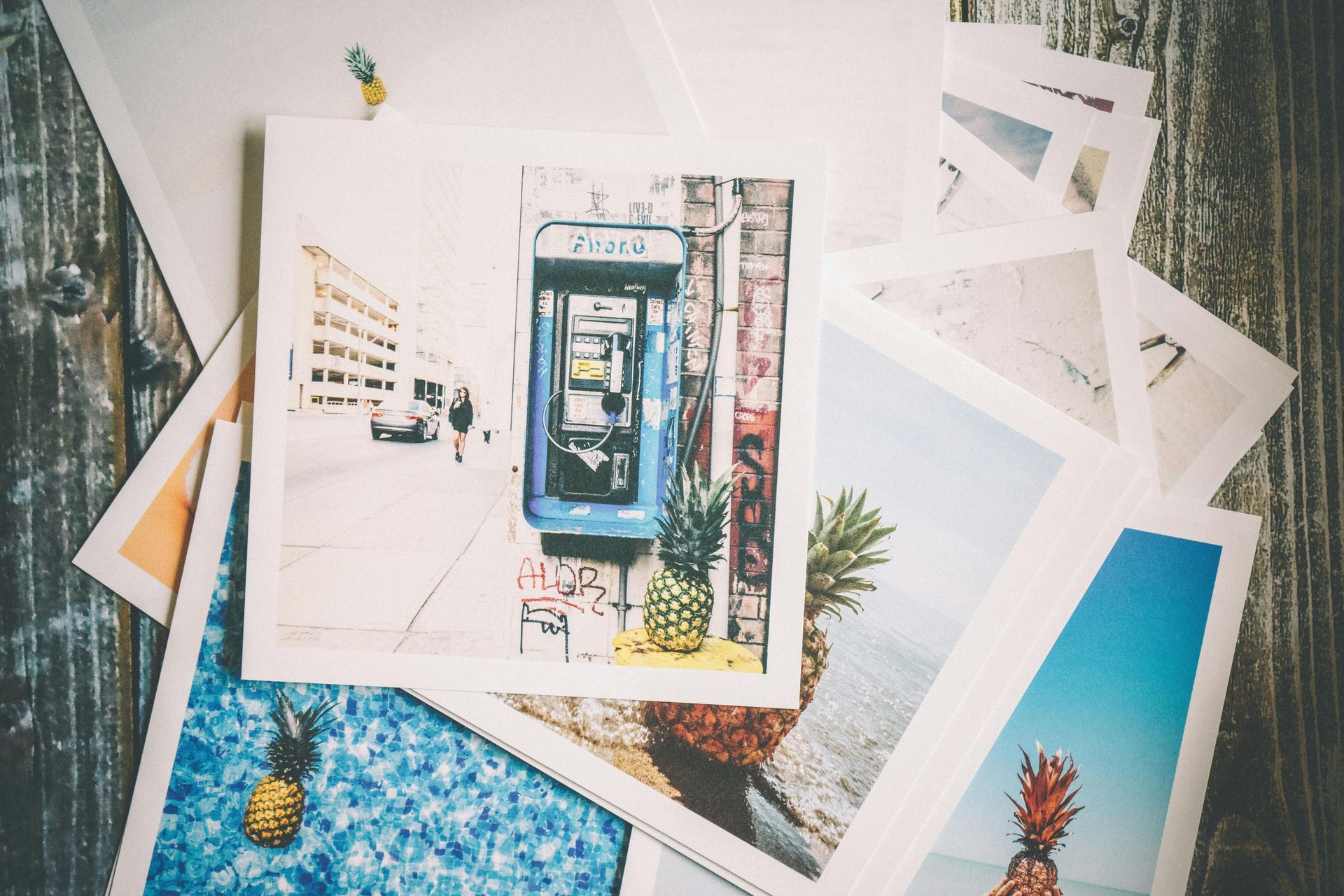 Photos scattered on a wooden surface: a blue phone booth, pineapples, and ocean views.