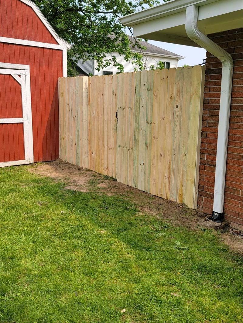 Wooden fence next to red shed and brick wall with white gutter.