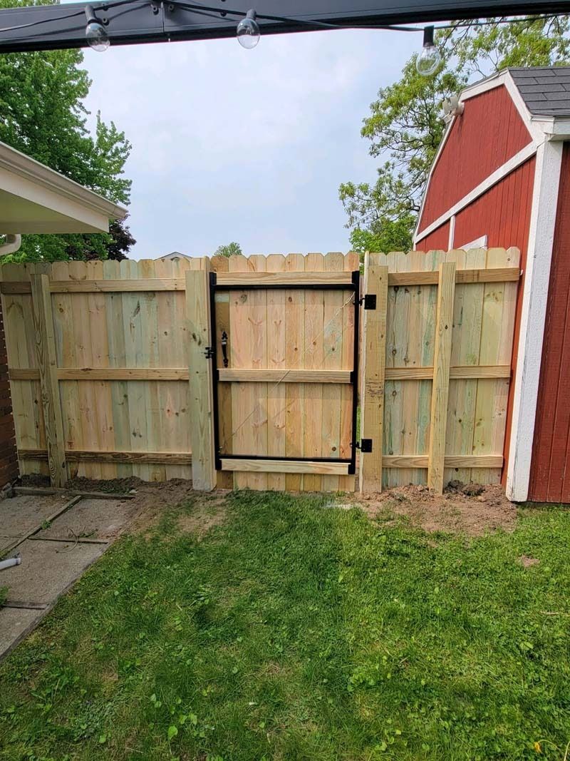 Wooden fence with a gate in a backyard; green grass in front, red shed to the right.