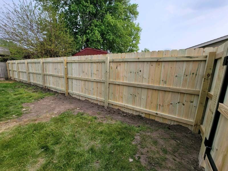 Wooden fence surrounding a yard, with green grass and trees in the background.