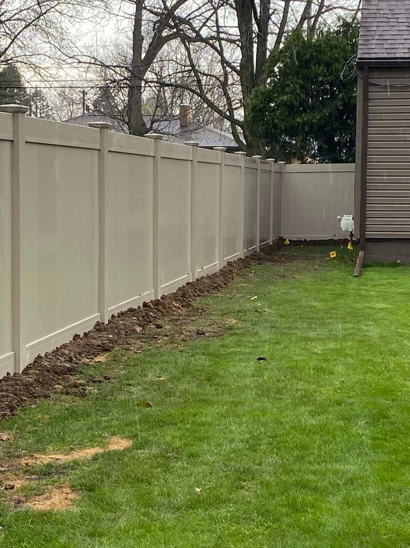 A beige vinyl fence bordering a green lawn. Dark soil borders the fence.