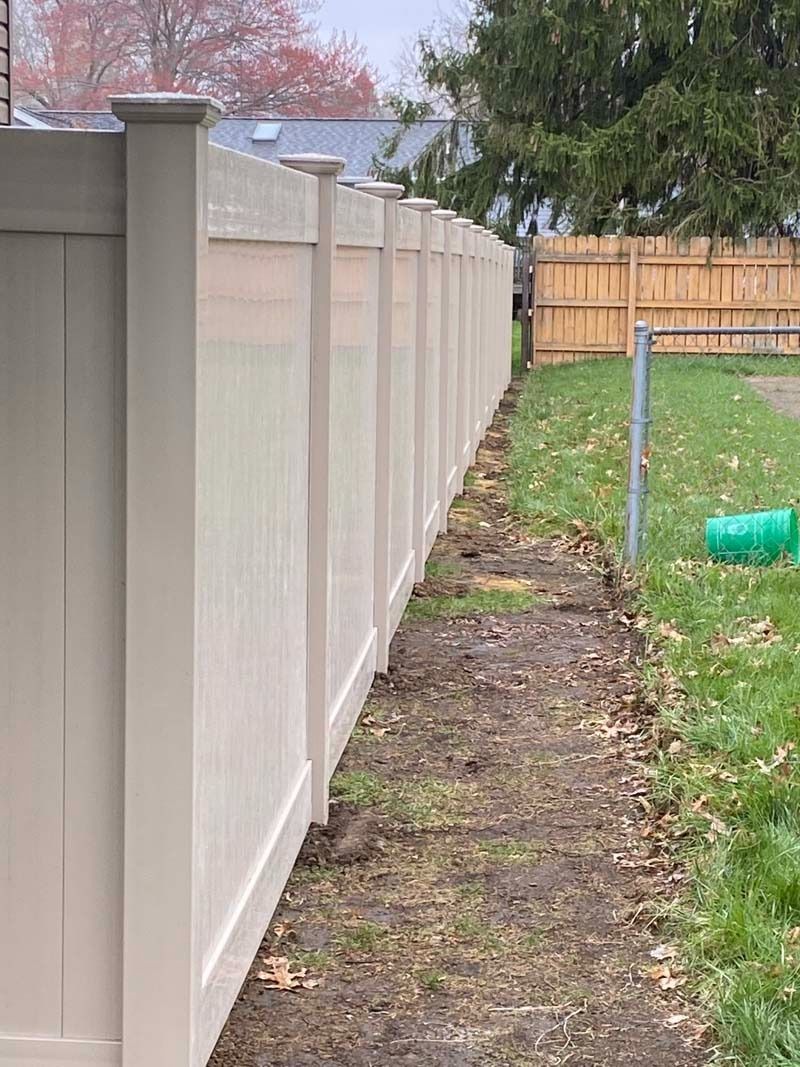 Beige vinyl fence along a grassy yard path, leading to a wooden fence in the distance.