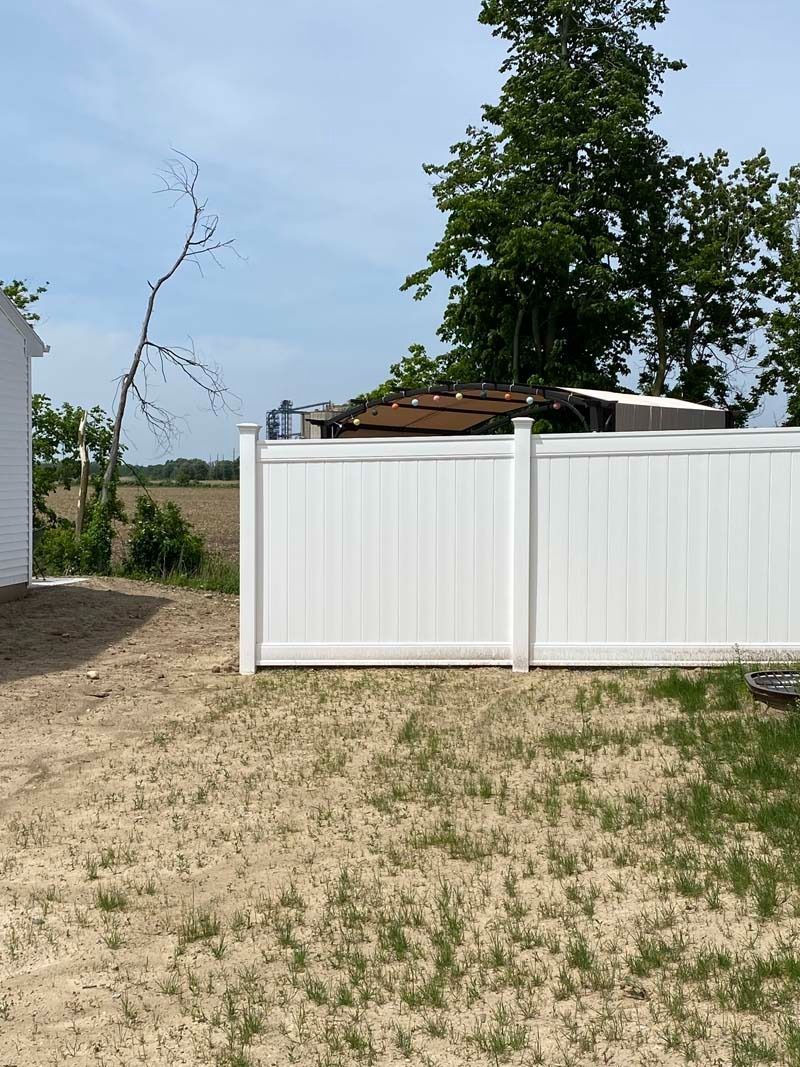White vinyl fence, dry grass in foreground, blue sky.