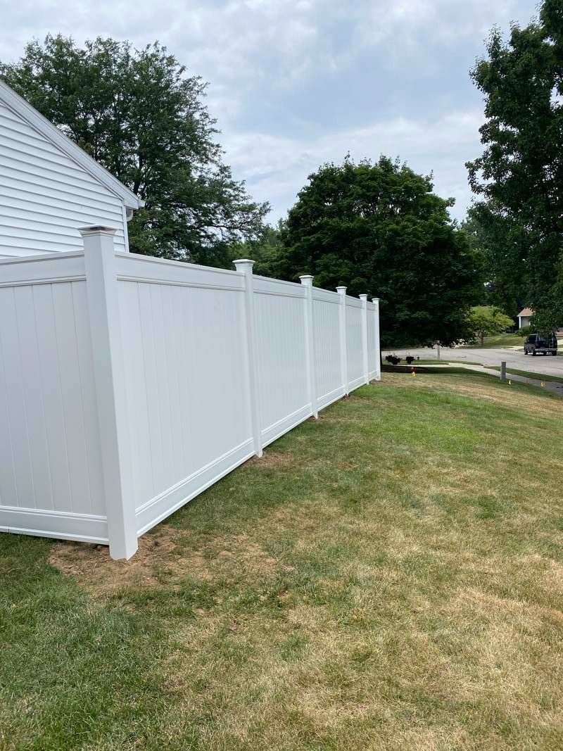 White vinyl fence in front yard; cloudy sky, green trees in background.