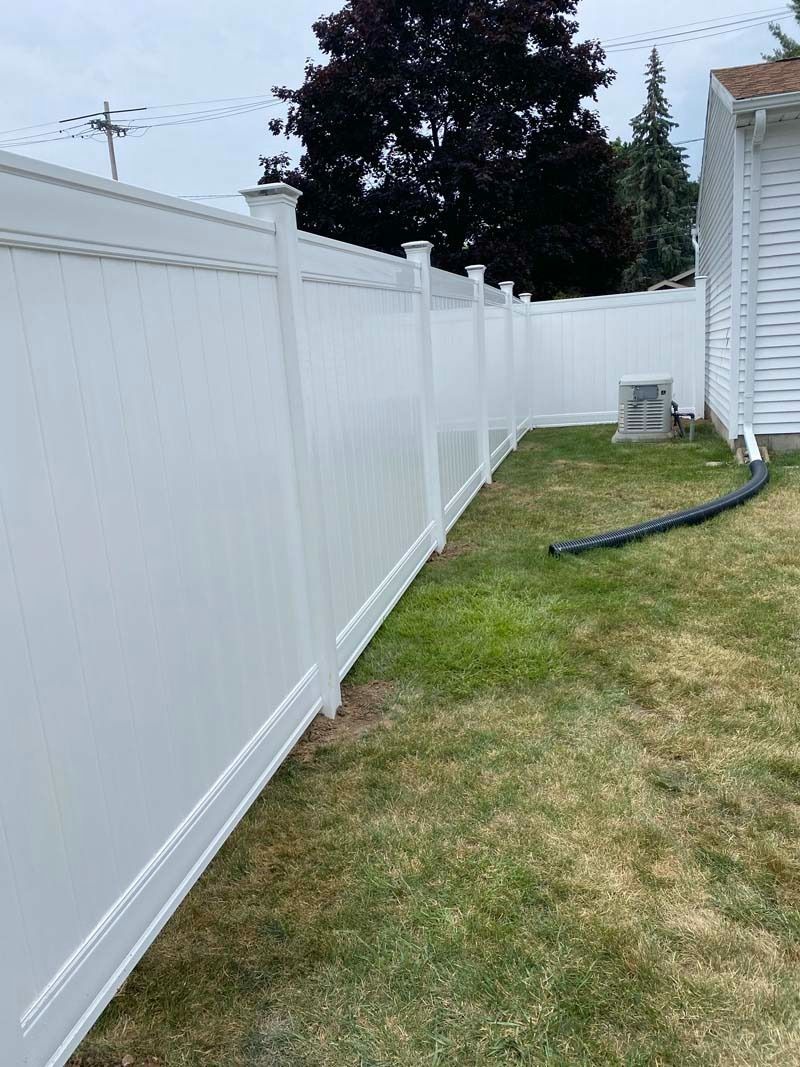 White vinyl fence in a grassy backyard.