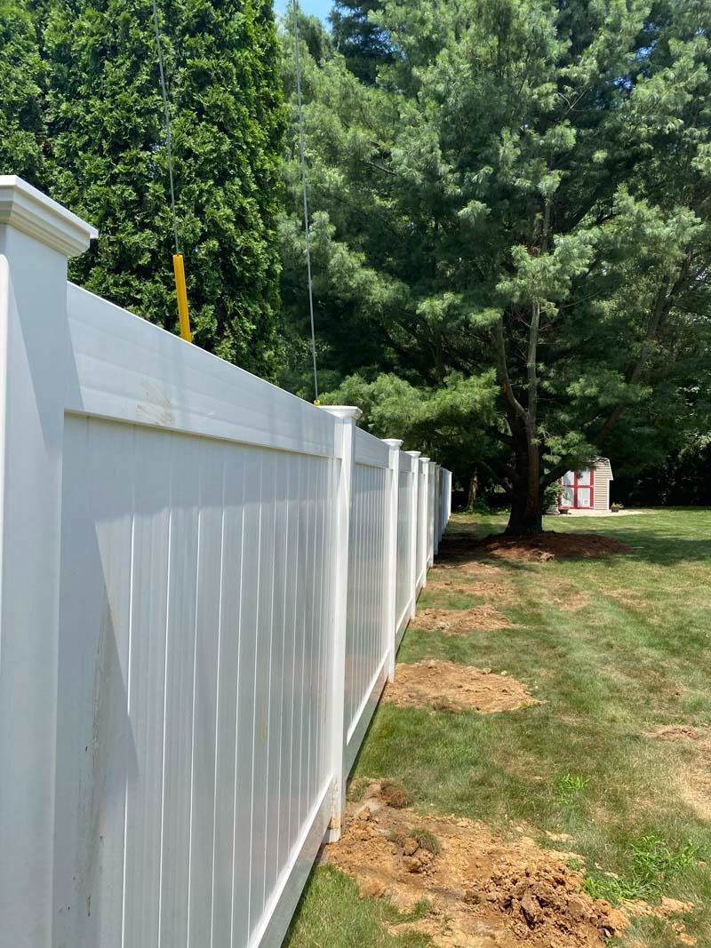 White vinyl fence in a grassy yard, with trees in the background under a sunny sky.