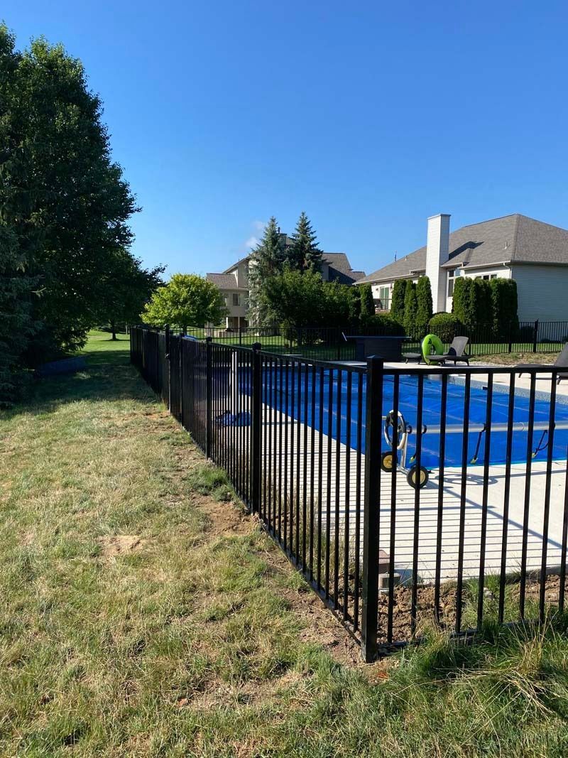Black metal fence surrounding a pool on a sunny day. Houses in the background.