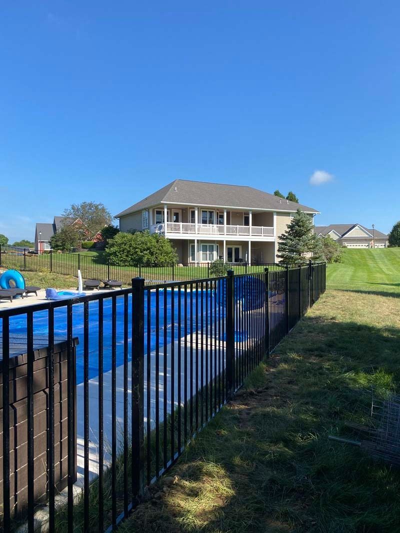 Black fenced pool in front of a large house on a sunny day.