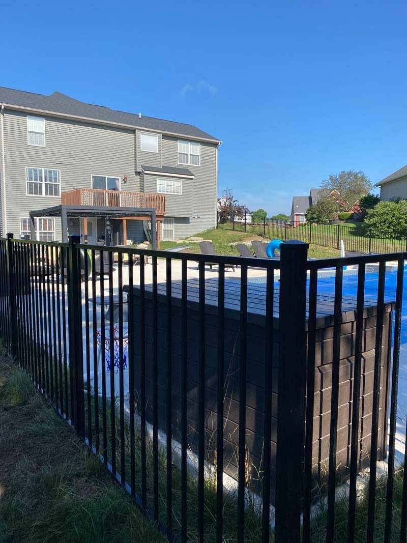 Black fence surrounds a pool. A two-story gray house is in the background on a sunny day.