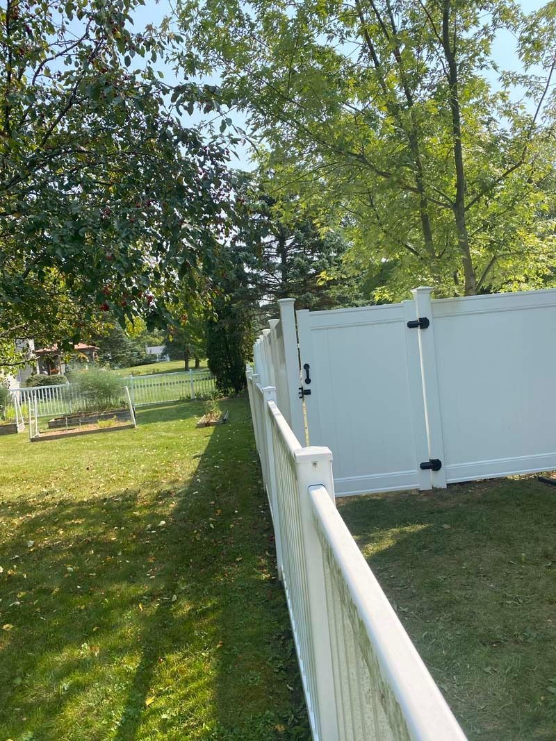 White fence and gate in a yard; trees and green grass.