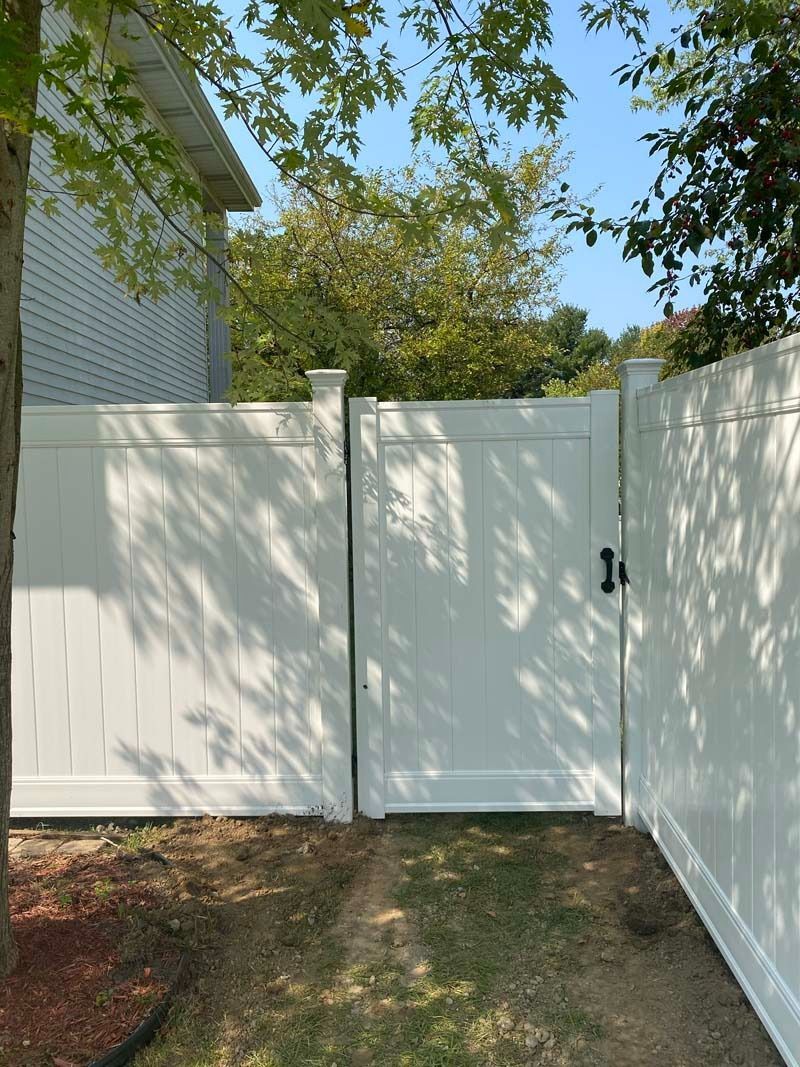 White vinyl fence and gate in a yard with trees.