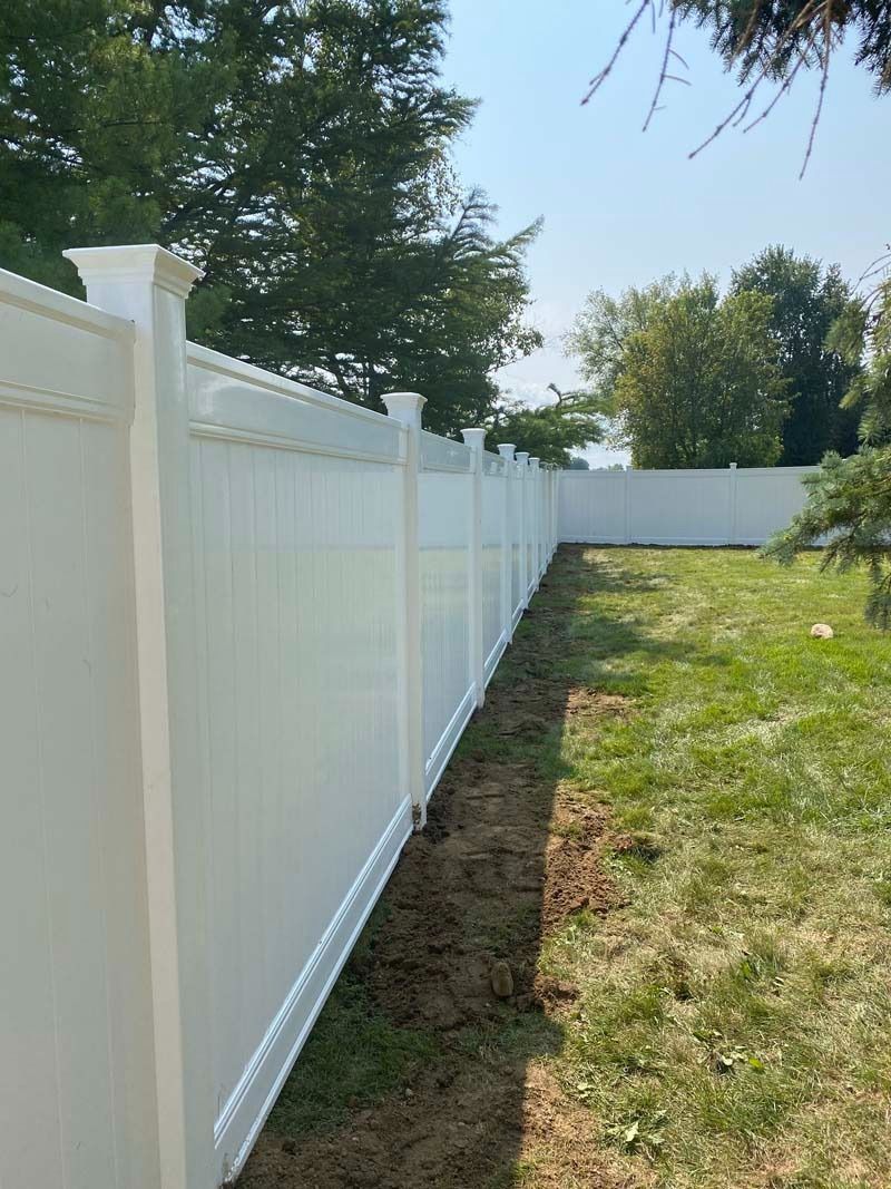 White vinyl fence along a grassy yard on a sunny day.