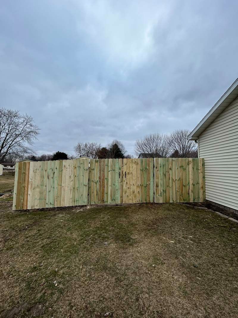 Wooden fence next to a house, in a grassy yard under a cloudy sky.