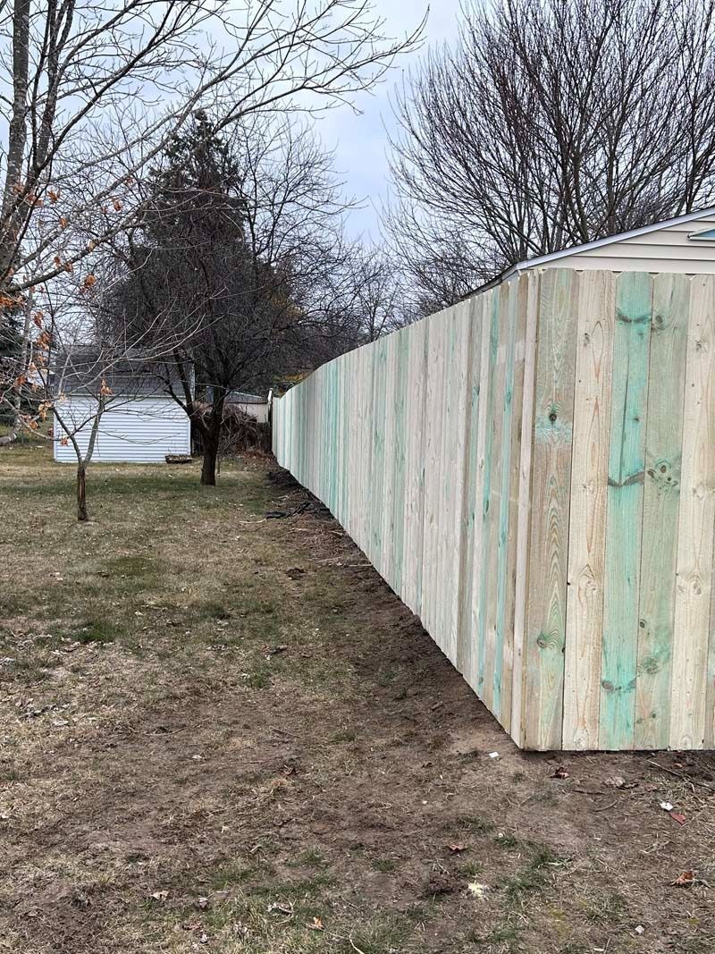 Wooden fence curving along a yard. The boards are light green and natural wood.