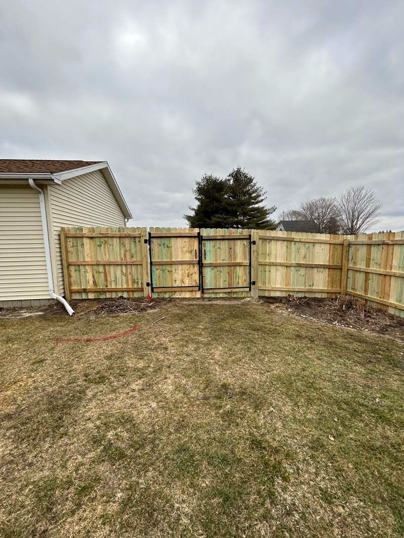 Wooden fence surrounding a grassy yard. Includes a gate near a siding house. Cloudy sky.