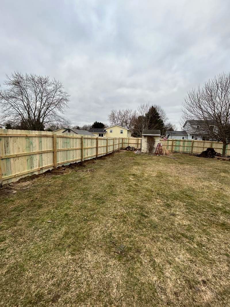 A backyard enclosed by a wooden fence under a cloudy sky.