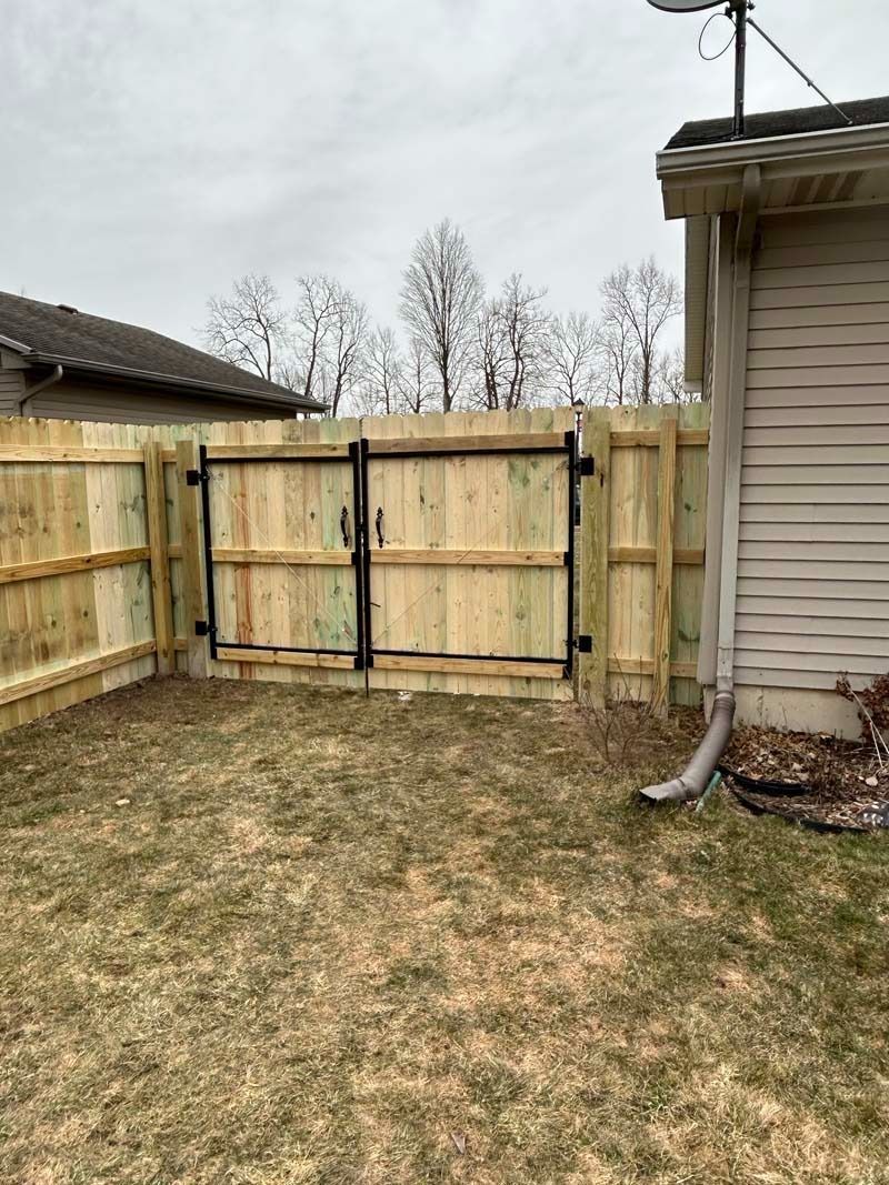 Wooden backyard fence with double gate; dry grass.
