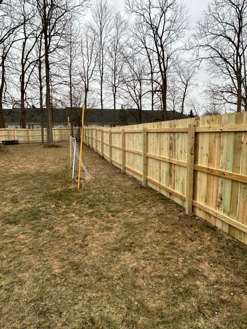Wooden fence in a grassy backyard, trees in the background, overcast sky.