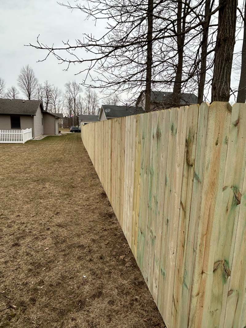 Wooden fence along a grassy yard with houses in the background on a cloudy day.