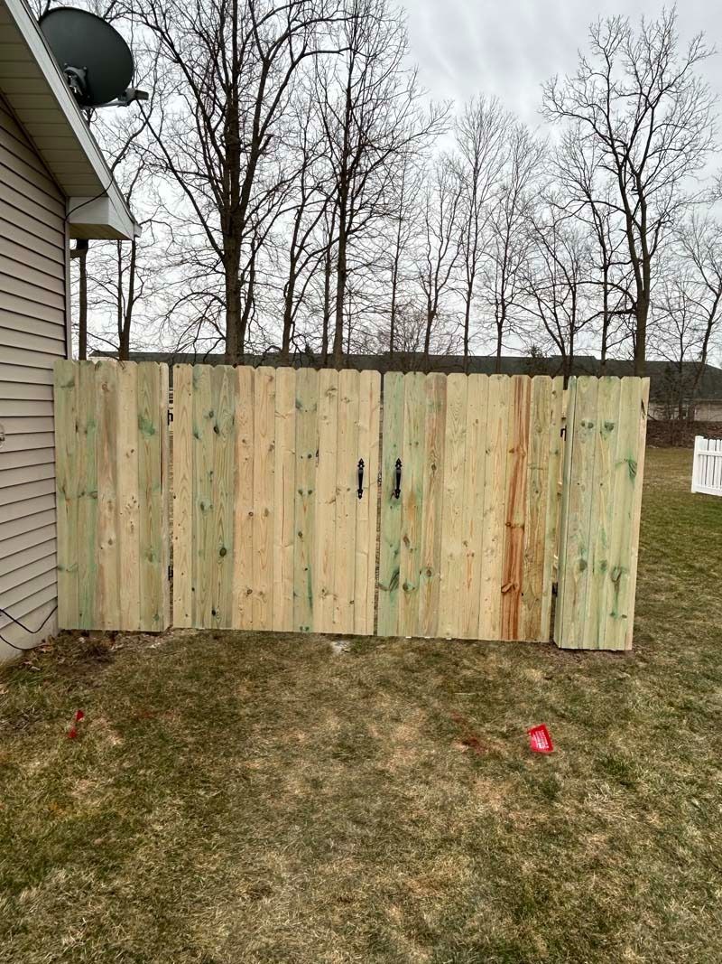 Wooden fence in a yard next to a house; trees in the background.