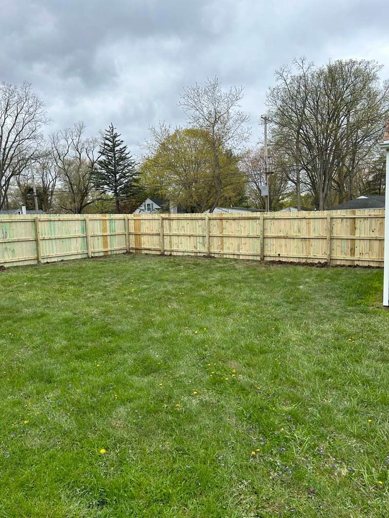 Green backyard with wooden fence under cloudy sky.