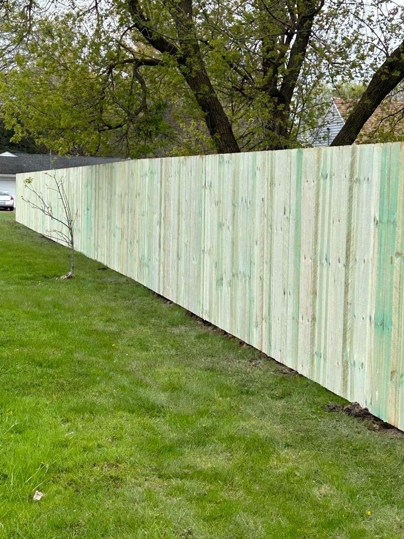 Green wooden fence along a grassy lawn with a tree in the background.