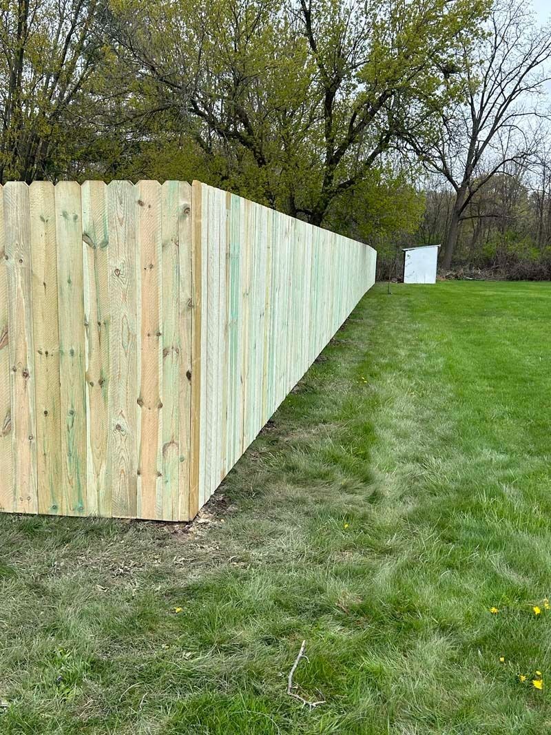 Wooden fence bordering a grassy lawn, trees in the background on a cloudy day.