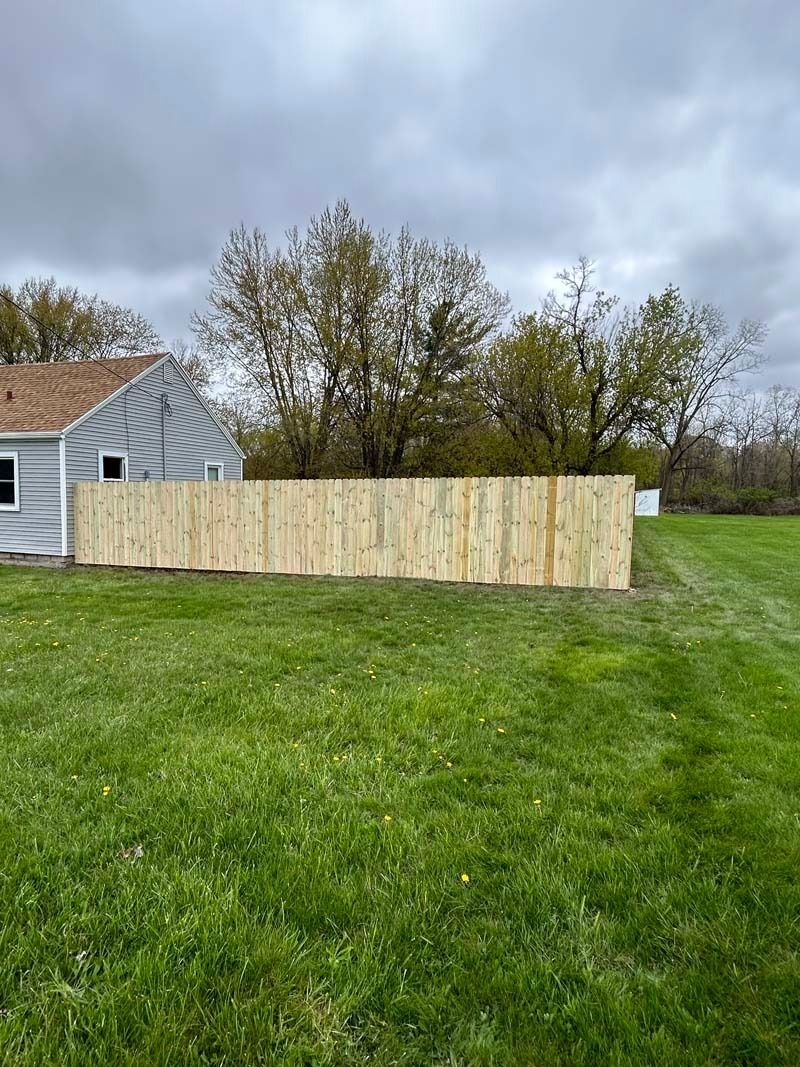 Wooden fence in front of a house on a green lawn under a cloudy sky.