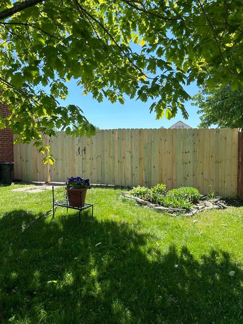 Backyard scene with green grass, wooden fence, and a pot of flowers.