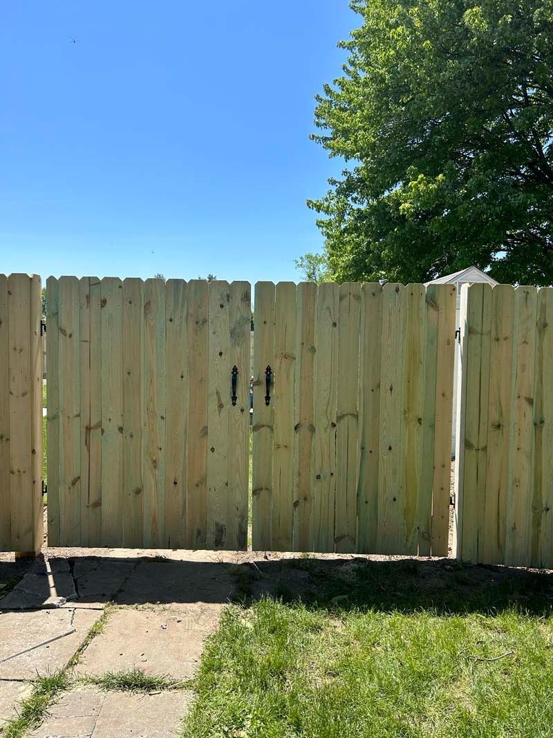 Wooden gate in a wooden fence, with black handles. Sunny day, green grass.