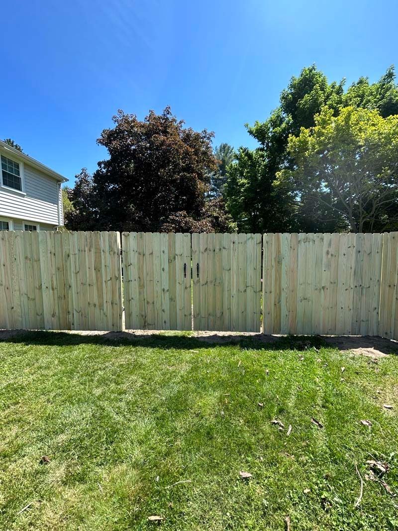 Wooden fence with closed gate against a blue sky and trees in a backyard.
