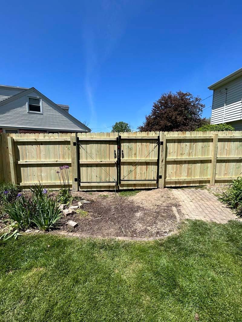 Wooden fence with gate in a backyard, with a clear blue sky.