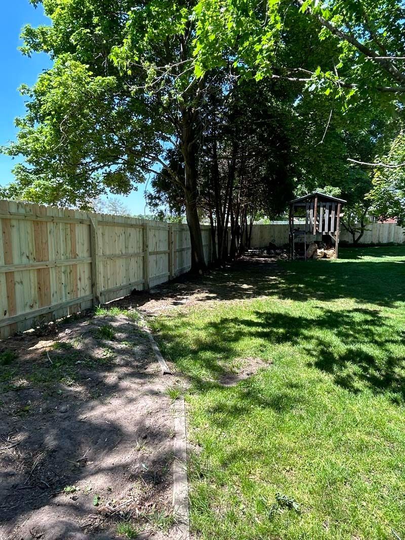 A backyard with a new wooden fence, trees, and a small playhouse under a sunny sky.