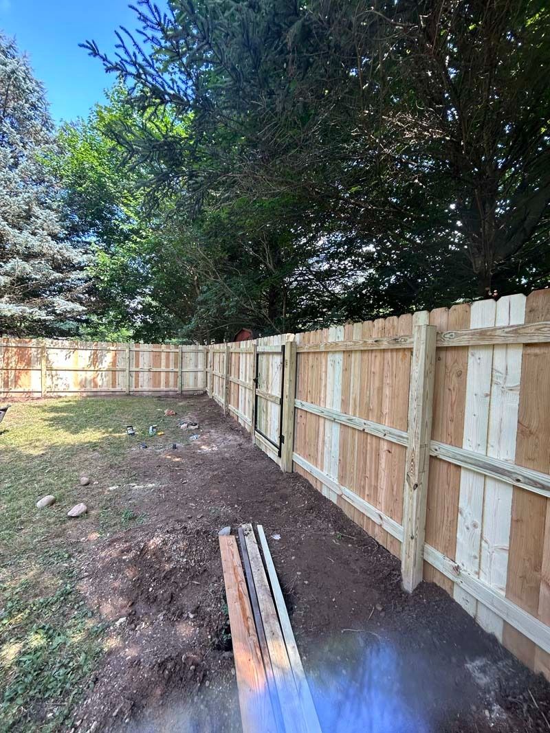A wooden fence surrounds a backyard. Brown posts and panels, green grass, and a dirt path.