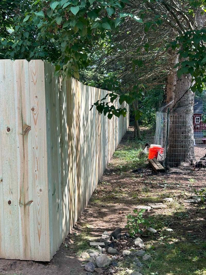 New wooden fence borders a shaded yard with a tree and debris.
