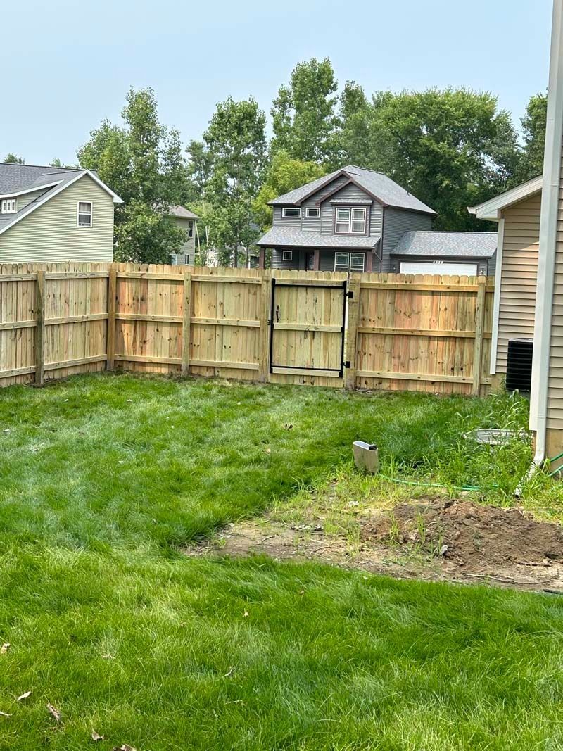 Wooden fence encloses a grassy backyard. A multi-story house is visible in the background.