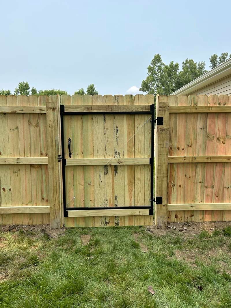 Wooden fence with a black gate set in green grass.