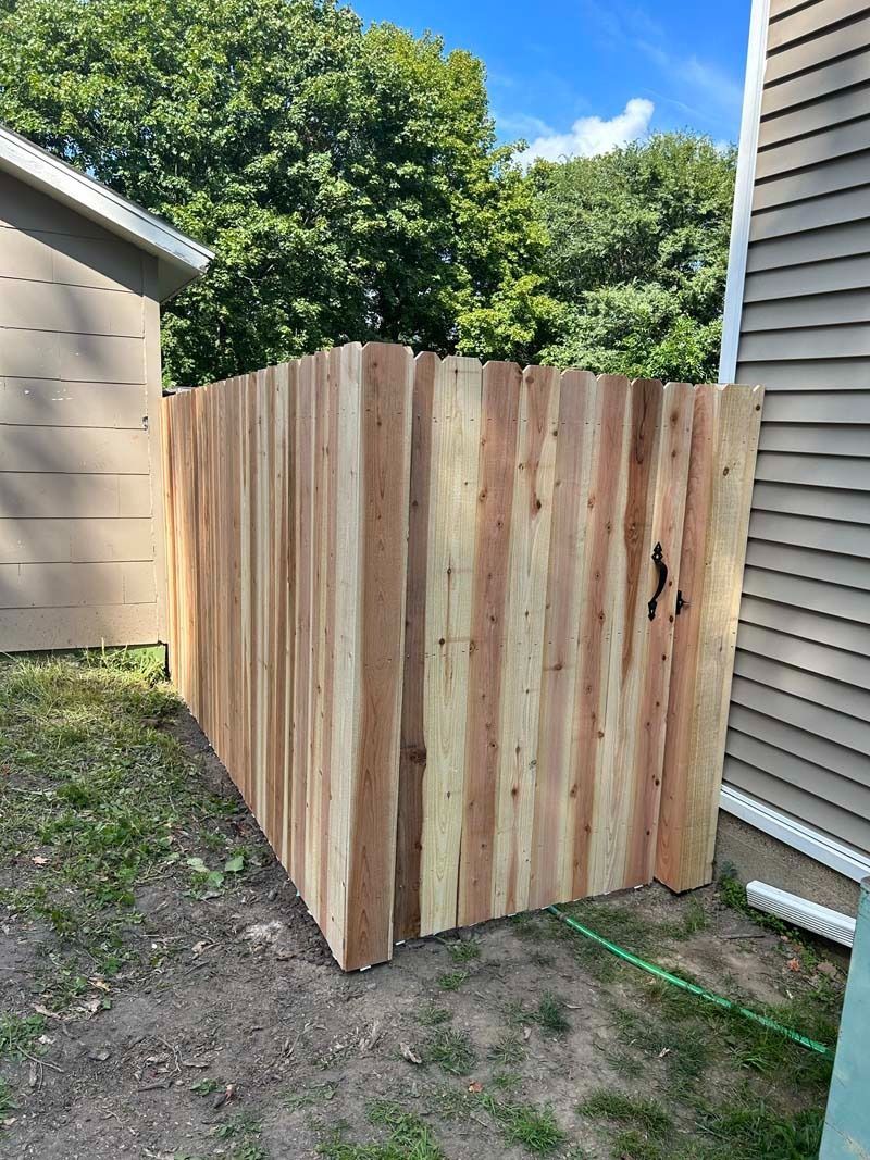 Wooden privacy fence against the side of a house. Brown cedar planks in a fenced yard.