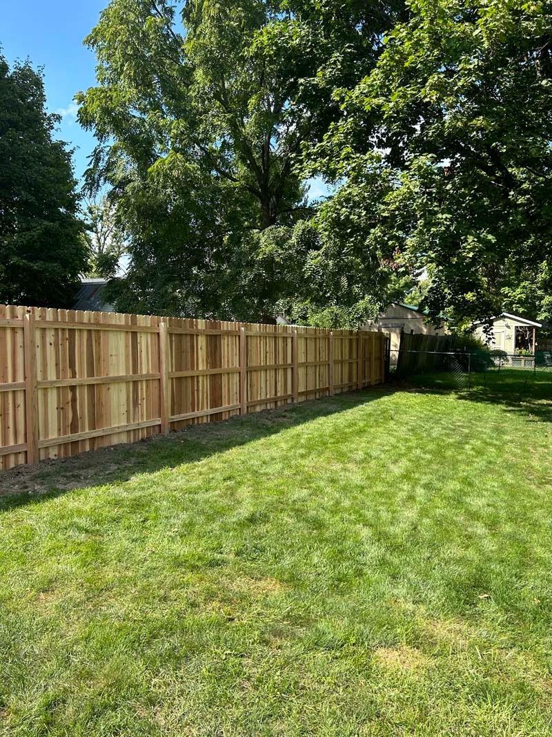 Wooden fence along a green lawn with a large tree in the background. Sunny day.